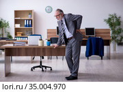 Old male employee suffering from radiculitis at workplace. Стоковое фото, фотограф Elnur / Фотобанк Лори