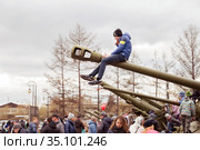 Boy is sitting on the artillery gun barrel, which stand near the museum of the Victory Memorial during the celebration of Victory Day WWII. Krasnoyarsk. Krasnoyarsk Region. Russia. (2018 год). Редакционное фото, фотограф Светлана Попова / Фотобанк Лори