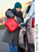 Positive adult woman a driver pouring petrol from red plastic gasoline can into a car tank on the road. Стоковое фото, фотограф Кекяляйнен Андрей / Фотобанк Лори