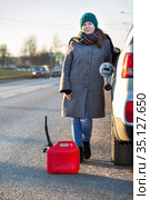 Woman a driver standing on the road leaning her suv with empty plastic can on asphalt, opened car-tank cap, winter season. Стоковое фото, фотограф Кекяляйнен Андрей / Фотобанк Лори