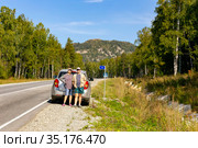 a man and a woman autotourists stand on the highway near the car and point to the high mountain Aleksandrovskaya Sopka on a sunny summer day. Стоковое фото, фотограф Акиньшин Владимир / Фотобанк Лори