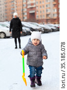 Joyful pretty toddler child running from mother with shovel toy, winter season, people walk on urban parking lot. Стоковое фото, фотограф Кекяляйнен Андрей / Фотобанк Лори