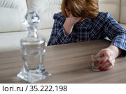 Drunk woman with a glass of vodka and a decanter covers her face with her hand. Стоковое фото, фотограф Володина Ольга / Фотобанк Лори