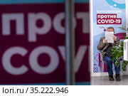 Мужчина читает анкету в очереди в мобильном пункте вакцинации от новой коронавирусной инфекции COVID-19 вакциной Спутник V в ГУМе города Москвы, Россия (2021 год). Редакционное фото, фотограф Николай Винокуров / Фотобанк Лори