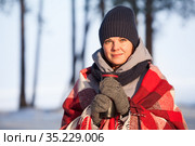 Portrait of young beautiful woman in winter clothes, red scarf and mittens holding thermo cup with hot beverage standing in sunny cold forest. Стоковое фото, фотограф Кекяляйнен Андрей / Фотобанк Лори