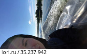 Vertical video of Caucasian woman sitting inside of moving motorboat. Selfie view with part of face and track on water and nature. Стоковое видео, видеограф Кекяляйнен Андрей / Фотобанк Лори