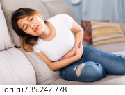 Mexican female at sofa holding hands on the illness stomache. Стоковое фото, фотограф Яков Филимонов / Фотобанк Лори