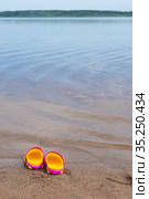 Детские розовые сабо стоят на песчаном пляже около воды. Children's pink clogs stand on a sandy beach near the water. Стоковое фото, фотограф Мария / Фотобанк Лори