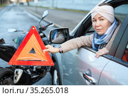 Woman a driver holding triangle sign is in her hand, sitting in car after road collision with motorcycle. Стоковое фото, фотограф Кекяляйнен Андрей / Фотобанк Лори