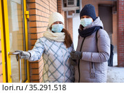 Two Caucasian women ready to enter the door of shop or store, females wearing medical mask to protect coronavirus infection. Safety rules for public place. Стоковое фото, фотограф Кекяляйнен Андрей / Фотобанк Лори