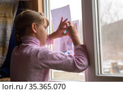 Девочка копирует напечатанную картинку на чистый лист, приложив картинку к стеклу окна. Стоковое фото, фотограф Иванов Алексей / Фотобанк Лори