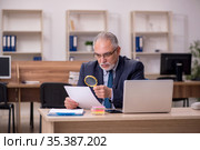 Old male employee auditor holding loupe at workplace. Стоковое фото, фотограф Elnur / Фотобанк Лори