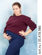 Excited brunette pregnant woman in brown cardigan and blue skirt touching belly on background. Стоковое фото, фотограф Кекяляйнен Андрей / Фотобанк Лори