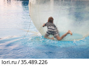 Little boy have fun inside big plastic balloon on the water of swimming pool on the summer resort. Kid inside big inflatable transparent ball running and having fun. Стоковое фото, фотограф Nataliia Zhekova / Фотобанк Лори