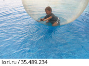 Little boy have fun inside big plastic balloon on the water of swimming pool on the summer resort. Kid inside big inflatable transparent ball running and having fun. Стоковое фото, фотограф Nataliia Zhekova / Фотобанк Лори