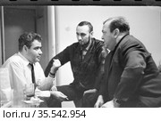 Трое мужчин беседуют сидя рядом со столом, человек в рубашке держит в руках сигарету и что-то объясняет приятелям, Чехословакия, 1960-е годы. Редакционное фото, фотограф Варфоломей Тетерин / Фотобанк Лори