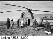Местные жители и доктор находятся на поляне рядом с вертолётом, посещение медиком отдалённых населённых пунктов с помощью санитарной авиации, Чукотка, 1960-е годы. Редакционное фото, фотограф Варфоломей Тетерин / Фотобанк Лори
