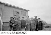 Коллективный портрет мужчины, ребенка и нескольких женщин позирующих стоя рядом с зданием, сотрудники птицефабрики под открытым небом, Лорино, Чукотка, 1970. Редакционное фото, фотограф Варфоломей Тетерин / Фотобанк Лори