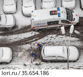 От  машины скорой помощи, с трудом припаркованной среди частных автомобилей в заснеженном дворе дома, идут врач и фельдшер. Сильный снегопад (2021 год). Редакционное фото, фотограф Наталья Николаева / Фотобанк Лори