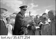 Мужчина зрелого возраста в форме пилот Аэрофлота жмёт руки встречающим его пионерам, лётчик держит цветы подаренные школьниками, фрагмент самолёта на заднем плане, Якутия, 1960. Редакционное фото, фотограф Варфоломей Тетерин / Фотобанк Лори