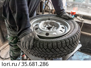 Мужчина в рабочей одежде и перчатках чинит колесо и заменяет зимнюю шину. Стоковое фото, фотограф Александр Бушков / Фотобанк Лори