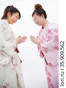 Two young smiling  woman in Japanese kimonos bowing to each other, studio shot. Стоковое фото, агентство Ingram Publishing / Фотобанк Лори