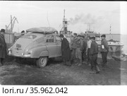 Несколько молодых людей находятся на берегу реки, они стоят рядом с автомашиной марки Победа, морское судно пришвартовано позади них, поездка Владивосток-Кронштадт, 1958. Редакционное фото, фотограф Варфоломей Тетерин / Фотобанк Лори