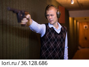 Man aiming smallbore sporting pistol at target in shooting range. Стоковое фото, фотограф Яков Филимонов / Фотобанк Лори