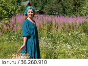 Young woman in folk peasant clothes on the background of a blooming meadow and rural buildings. Стоковое фото, фотограф Евгений Харитонов / Фотобанк Лори