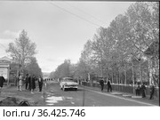 Центральная улица города Алдан, узкая дорога с автомобилем и множество пешеходов на обочинах, высокие деревья стоят по краям, Якутия, июнь 1965. Редакционное фото, фотограф Варфоломей Тетерин / Фотобанк Лори