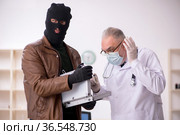Masked man burglar bribing old doctor for getting vaccine. Стоковое фото, фотограф Elnur / Фотобанк Лори
