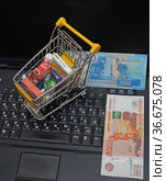 Концепция покупки продуктов питания через интернет. Игрушечная тележка для продуктов российские деньги на клавиатуре ноутбука (2021 год). Редакционное фото, фотограф Цибаев Алексей / Фотобанк Лори