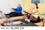 Woman pulling stretch band sitting on pilates training machin. Стоковое фото, фотограф Яков Филимонов / Фотобанк Лори