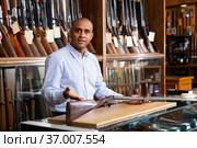 Hispanic salesman showing collectible rifled musket in gun store. Стоковое фото, фотограф Яков Филимонов / Фотобанк Лори
