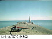 Гражданский вертолет вблизи белого маяка, скалистое побережье на фоне водной глади, голубое небо на заднем плане, мыс Дежнева, Чукотка, 1970 год. Стоковое фото, фотограф Варфоломей Тетерин / Фотобанк Лори