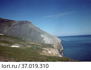 Морское побережье с отвесными скалами, горный берег омывается водами Берингова пролива, голубое небо над водной гладью, мыс Дежнева, Чукотка, 1970. Стоковое фото, фотограф Варфоломей Тетерин / Фотобанк Лори