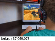 Игроман. Мальчик в наушниках играет в компьютерную игру перед монитором персонального компьютера. Стоковое фото, фотограф Гребенев Пётр / Фотобанк Лори