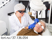 Focused cosmetologist performing laser resurfacing to senior woman. Стоковое фото, фотограф Яков Филимонов / Фотобанк Лори