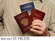 Смена гражданства, двойное гражданство, паспорта гражданина России, Донецкой Народной Республики  и Украины в руках мужчины (2022 год). Редакционное фото, фотограф Короленко Елена / Фотобанк Лори