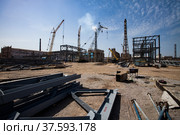 Mobile cranes and factory chimney on blue sky with clouds. Grey metal elements laying on ground. Assembling of industrial buildings. Abstract construction site panorama. Стоковое фото, фотограф Alexey Rezvykh / Фотобанк Лори