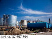 Oil Refinery and Gas processing plant. Shiny metal oil storage tanks and blue water storage tank on blue sky with clouds. Heap of ground for ground works. Jambyl, Kazakhstan. Стоковое фото, фотограф Alexey Rezvykh / Фотобанк Лори