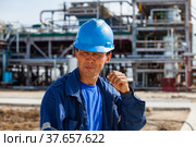 Taraz, Kazakhstan - April 25 2012: Asian oil worker in blue work wear and blue hardhat on oil refinery plant blurred background. Редакционное фото, фотограф Alexey Rezvykh / Фотобанк Лори