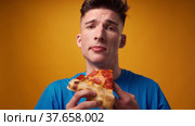 Close up of a guy eating pizza slice against yellow studio background. Стоковое видео, видеограф Сергей Толмачёв / Фотобанк Лори