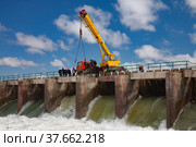 Kok-aral, Kazakhstan - May 03, 2012: Small Aral Sea Kok-aral dam. Water discharge in flood. Open shutters. Yellow mobile crane and workers on dam. Стоковое фото, фотограф Alexey Rezvykh / Фотобанк Лори