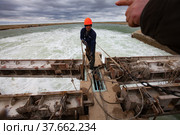 Kok-aral, Kazakhstan - May 03, 2012: Small Aral Sea Kok-aral dam. Worker in orange hardhat use steel rope to lifting water shutter weighting agent. Редакционное фото, фотограф Alexey Rezvykh / Фотобанк Лори