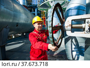 Aktobe region/Kazakhstan - May 04 2012: Oil refinery plant. Maintenance worker in red work wear and yellow hardhat adjusting technological steering wheel. CNPC-AMG company. Редакционное фото, фотограф Alexey Rezvykh / Фотобанк Лори