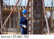 Aktau, Kazakhstan - May 19, 2012 Construction of modern asphaltic bitumen plant. Worker in white balaclava mask, and blue helmet assembling forms for filling. Reinforcement steel on background. Стоковое фото, фотограф Alexey Rezvykh / Фотобанк Лори