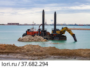 Mangystau, Kazakhstan - May 19, 2012: Construction of man-made island with excavator and self-propelled barge. Oil rig on horizon. Caspian Sea, Bautino bay, seaport. Стоковое фото, фотограф Alexey Rezvykh / Фотобанк Лори