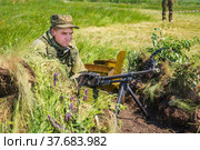 Russia, Samara, June 2019: A soldier in military uniform sits in ambush with a machine gun on a sunny summer day. Редакционное фото, фотограф Акиньшин Владимир / Фотобанк Лори