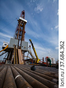 Uralsk region, Kazakhstan - May 24 2012: Oil deposit Zhaikmunai. Works on drilling rig. Rusted drilling pipes and oil worker on foreground. Blue sky and light clouds. Wide-angle photo. Редакционное фото, фотограф Alexey Rezvykh / Фотобанк Лори
